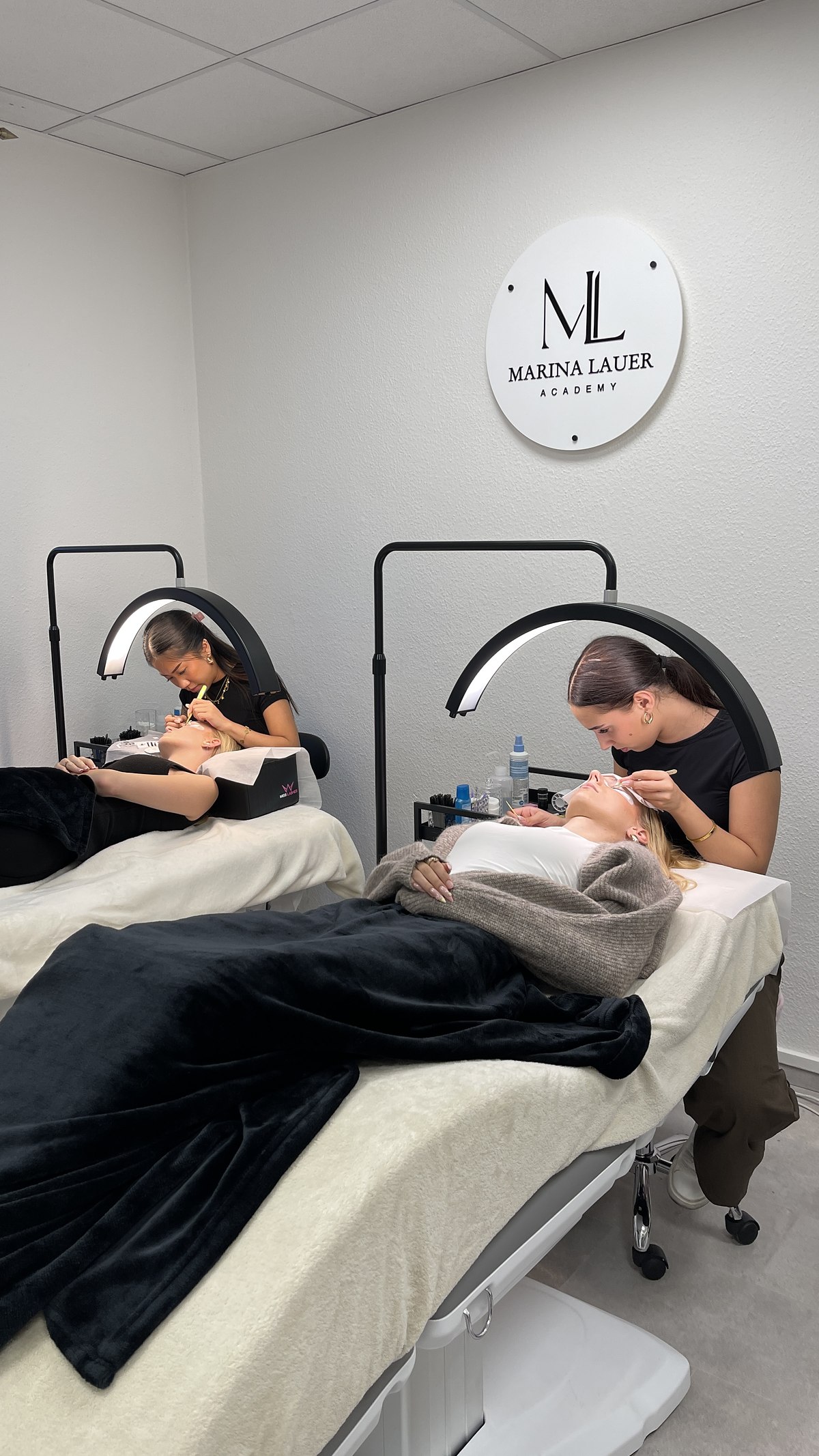 Zwei Teilnehmerinnen setzen Wimpern an Modellen im Behandlungsraum der Marina Lauer Academy